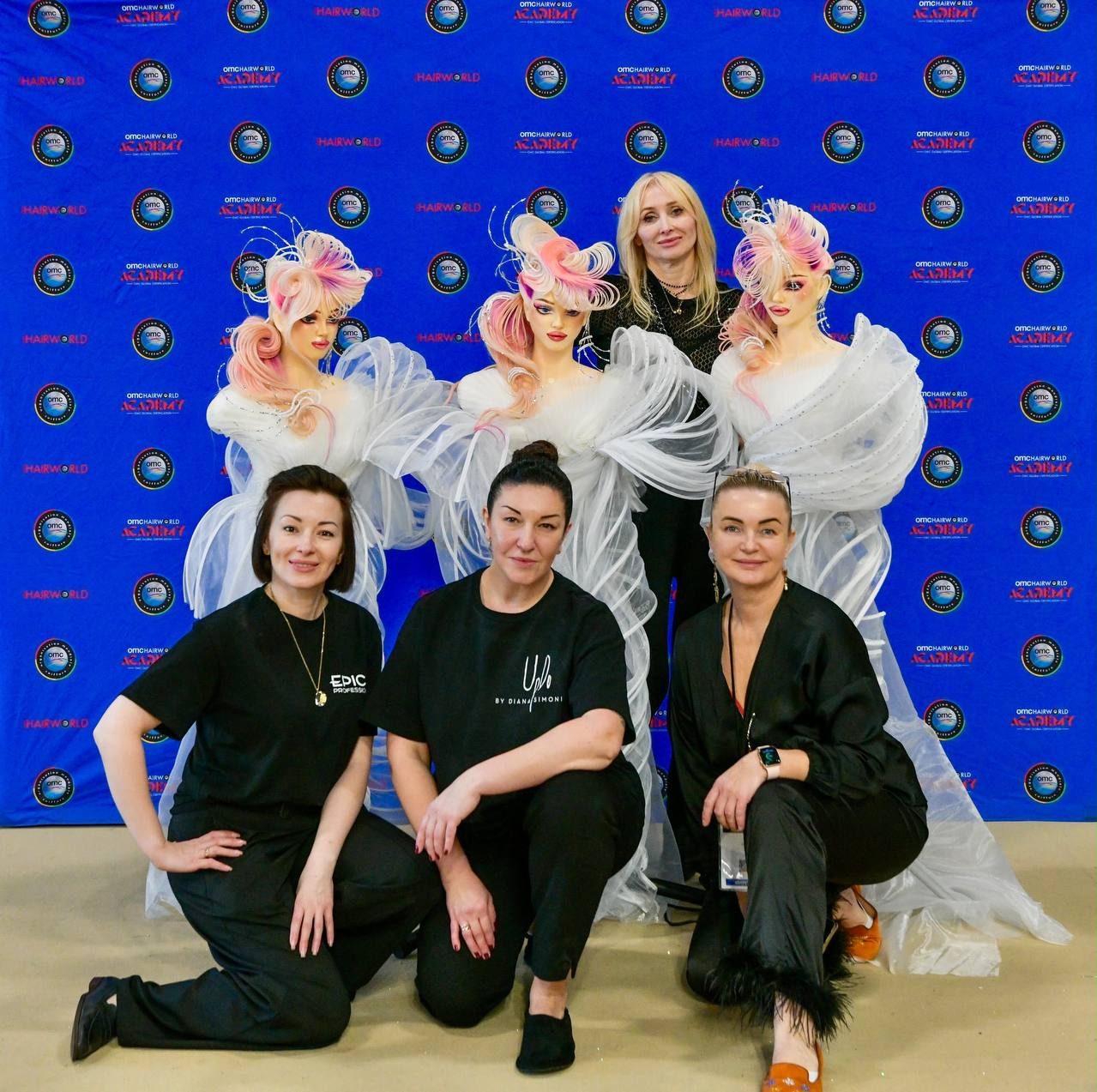 Участницы сборной у конкурсных работ на фоне баннера Hairworld