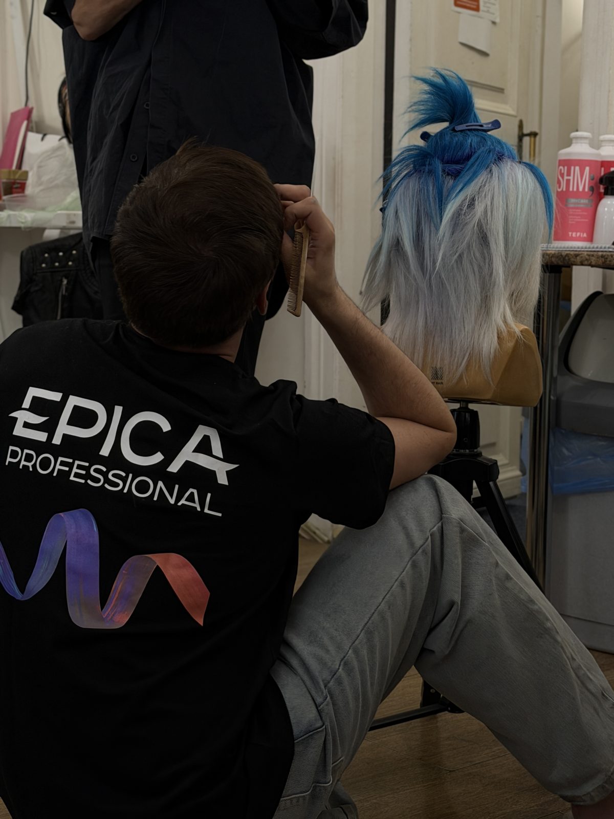 Мастер в футболке EPICA Professional за работой над конкурсной причёской на манекене